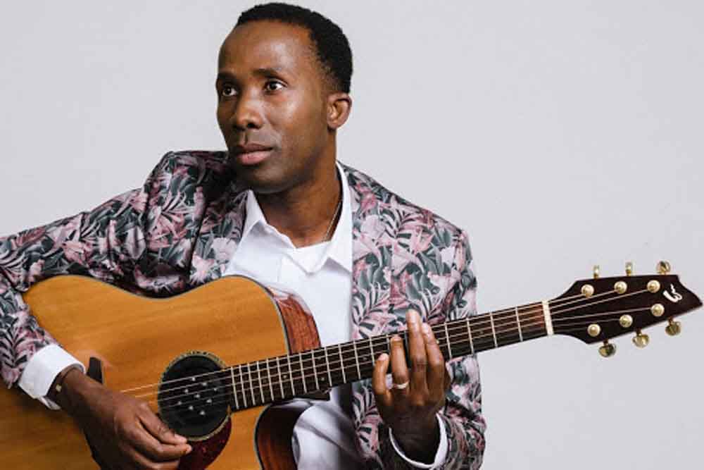 BélO avec son instrument de musique, guitariste et compositeur haïtien